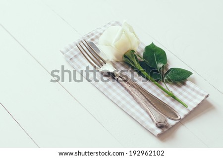 Vintage cutlery, antique silverware, fork, knife and a rose flower with rough cloth on an white painted wooden background