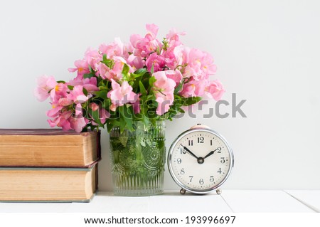 Retro home decor: a stack of books, flowers and a vintage alarm clock on a white wall shelf