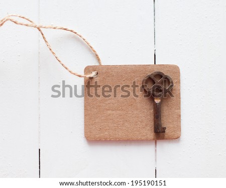 Empty brown cardboard tag on rough rope and rusty antique key on a white wooden board
