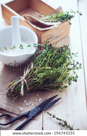 Cozy rustic home kitchen still life, dried herbs thyme, salt in white mortar, old wooden box and vintage scissors on the table.