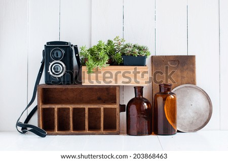 Vintage home decor: old wooden boxes, houseplants, camera and old brown glass bottles on white wooden board, retro home interior.