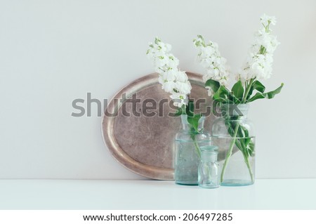 Vintage home decor, white matthiola flowers in different blue glass bottles vases and an antique silver tray on a shelf by the wall