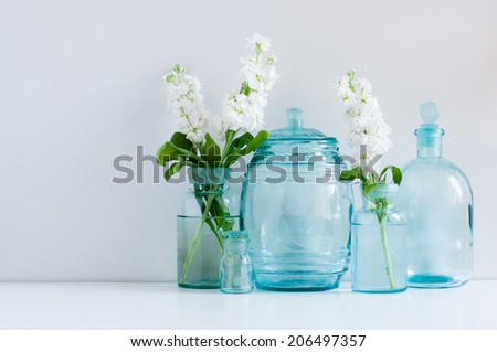 Vintage home decor background, white matthiola flowers in different blue glass bottles vases and antique jars on a shelf by the wall