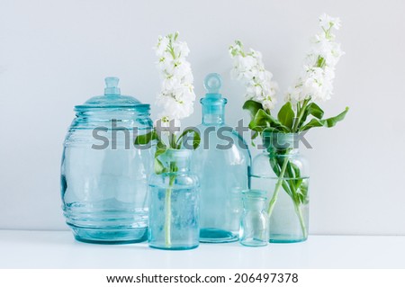 Vintage home decor, white matthiola flowers in different blue glass bottles vases and antique jars on a shelf by the wall