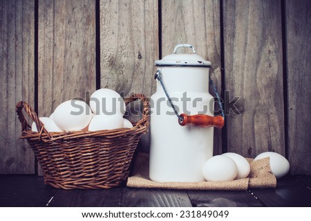 Country kitchen Still Life, enamel milk can, eggs in a wicker basket and wooden spoons on a background of the old board, vintage style