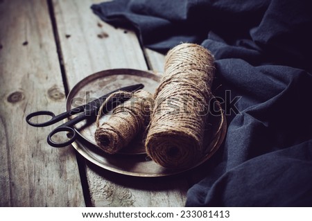Vintage still life, old scissors, cupronickel trays, dark cloth and a few skeins of rough rope on a wooden board