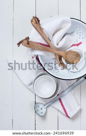 Rustic kitchen decor, enameled colander, wooden spoons and linen towels, dishes on a white board