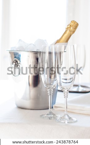 A bottle of chilled champagne in an ice bucket and two glasses on a white tablecloth, luxurious celebration, bright daylight