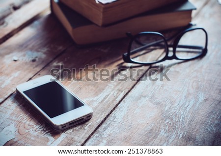 Old vintage books, smartphone and glasses on a wooden table