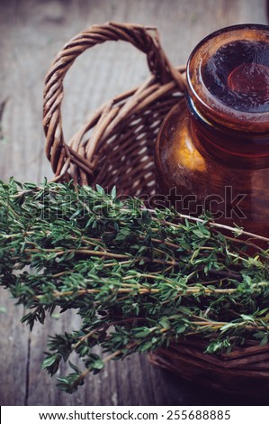 Brown glass pharmacy bottle and thyme herb in a wicker basket vintage style on old wooden board.