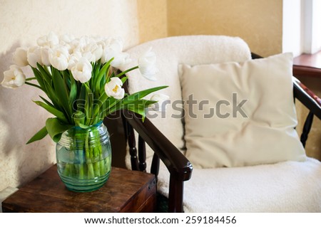 Home interior, vintage chair with a pillow and a bouquet of white tulips