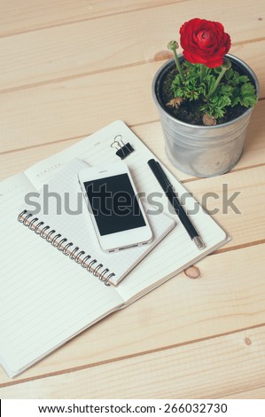 Rustic tabletop, home office: notebooks, smart phone, pen and a flower