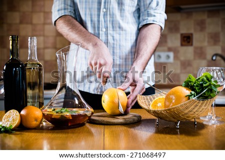 Man cuts fresh grapefruits for making sangria for home party, home kitchen interior. Homemade food and drinks