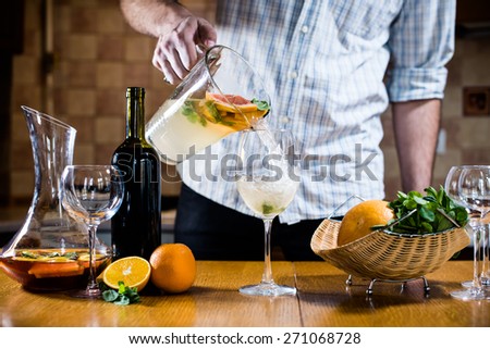 Man pours white homemade sangria with fruit pieces in a glass. Refreshing summer drinks