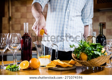 The man squeezes orange juice in a decanter for the preparation of sangria for home party, home kitchen interior. Homemade food and drinks