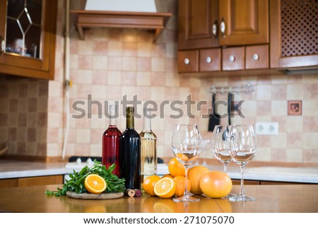 Three bottles of wine: white, rose and red, empty glasses and fruits on the kitchen table in a home kitchen interior