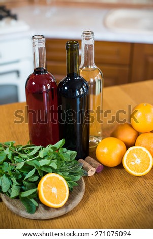 Three bottles of wine: white, rose and red, empty glasses and fruits on the kitchen table in a kitchen interior, closeup