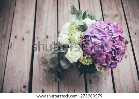 Big bouquet of fresh flowers, purple hydrangeas and white roses in a wicker basket on an old wooden board, vintage style