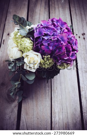 Big bouquet of fresh flowers, purple hydrangeas and white roses in a wicker basket on an old wooden board, vintage style