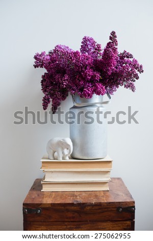 Home interior decor, bouquet of lilacs in a vase and books on rustic wooden table, on a white wall background