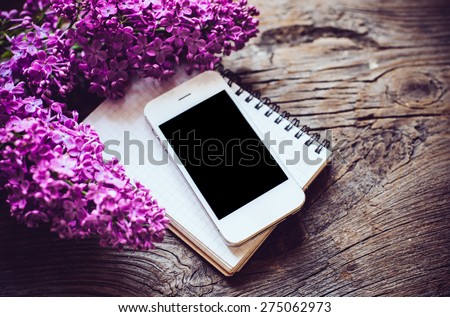 Books, notebooks, vintage style, white smart phone and lilac flowers on an old wooden board background, hipster lifestyle