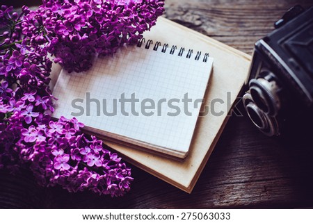 Books, notebooks, vintage camera and lilac flowers on an old wooden board background, hipster lifestyle composition