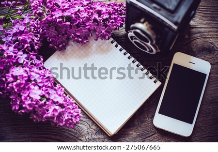 Books, notebooks, vintage camera, white smart phone and lilac flowers on an old wooden board background, hipster lifestyle arrangement