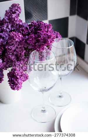 Spring bouquet of lilacs in a vase and glasses on the kitchen table by the wall, home interior