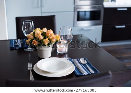 Simple home table setting with flowers, glasses and cutlery in the kitchen interior.
