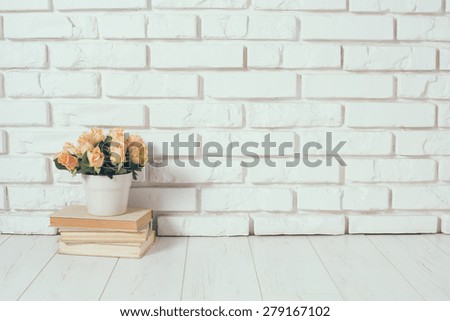 Roses in a vase and a stack of old vintage books on a  white brick wall background, room interior.