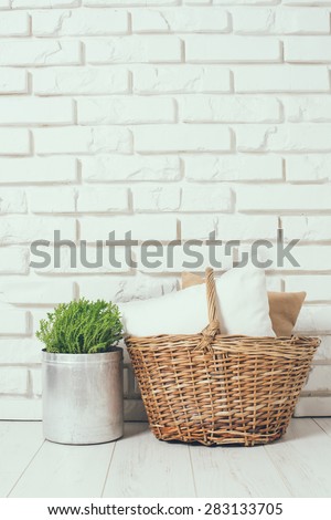 Wicker basket with a pillow and green home plant at the white brick wall on the floor, rustic home interior decor with copy space