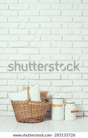 Wicker basket with a pillow and milk cans at the white brick wall on the floor, rustic home interior decor