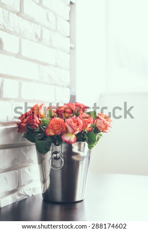 Bunch of fresh roses in a metal bucket for champagne on a table in a bright interior room