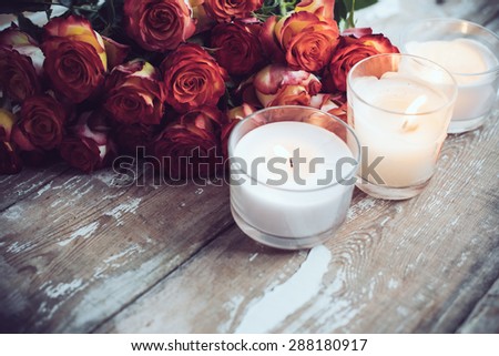 Vintage holiday decor, a bouquet of red roses and burning candles on an old wooden board surface, wedding decoration