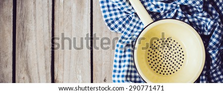 Yellow enamel colander and blue linen cloth on an old wooden board, rustic kitchen background.