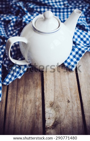 Large white porcelain teapot and a blue linen napkin on old wooden board, rustic kitchen background.