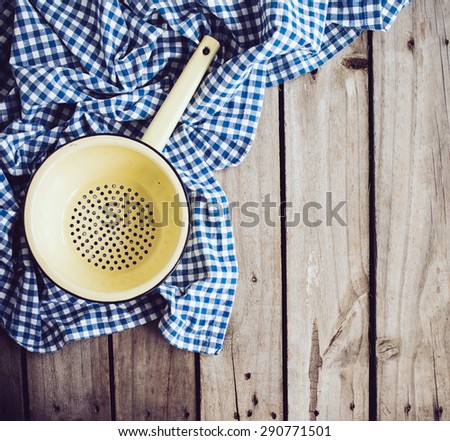 Yellow enamel colander and blue linen cloth on an old wooden board, rustic kitchen background.