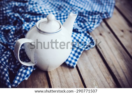 Large white porcelain teapot and a blue linen napkin on old wooden board, rustic kitchen background.