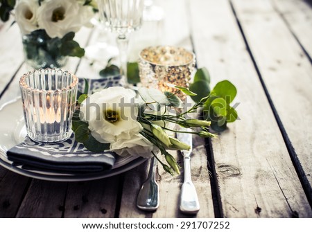 Table setting with white flowers, candles and glasses on old vintage rustic wooden table. Vintage summer wedding table decoration.