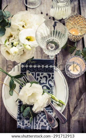 Table setting with white flowers, candles and glasses on old vintage rustic wooden table. Vintage summer wedding table decoration, top view.
