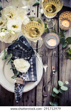 Table setting with white flowers, candles and glasses of champagne on an old vintage rustic wooden table. Vintage summer wedding table decoration, top view.