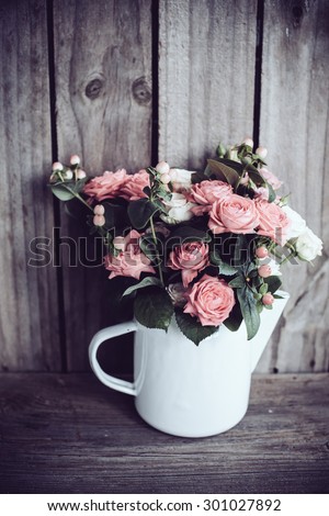 Bouquet of pink and beige roses in vintage enamel coffee pot on old wooden barn board background. Rustic flowers with copy space.