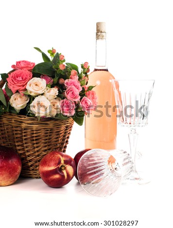 Fresh natural pink roses in a wicker basket  and a bottle of rose wine with two wineglasses and nectarines on white background isolated. Fruits, wine and flowers.