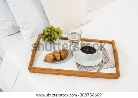 Breakfast in bed, tray with coffee, fruits and croissants on a bed with white linen in bedroom interior, hotel room