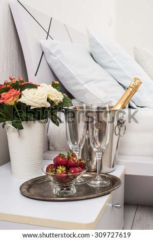 Champagne in bed in a hotel room, ice bucket, glasses and fruits on white linen