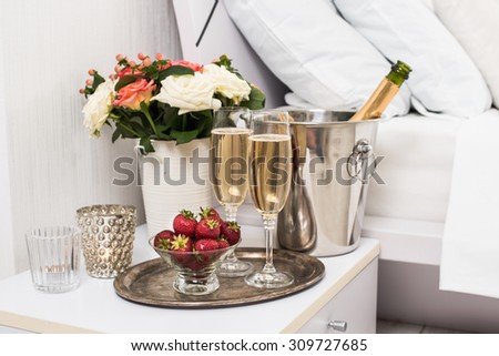 Champagne in bed in a hotel room, ice bucket, glasses and fruits on white linen