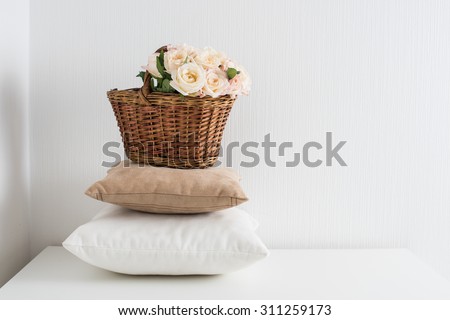 Basket with flowers on a pile of pillows by the white wall, a cozy home decor