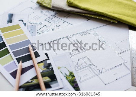 Interior designer\'s working table, an architectural plan of the house, a color palette, furniture and fabric samples in yellow and grey color. Drawings and plans for house decoration.