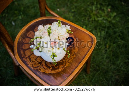 Summer wedding party festive decor, lovely fresh bouquet of white summer roses and freesias in vintage enamel tea pot on an old brown wooden chair. Retro style outdoor decoration, grass background.