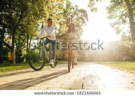 Young couple man and woman ride a bike in the park in the autumn season on a background of sunset. Cycling on the weekend with a friend. Imagine de stoc © 